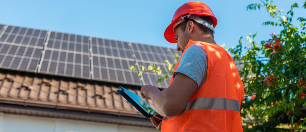 technicien qui vérifie une installation de panneaux photovoltaïque sur un toit de maison, prestation proposée par EDSC votre installateur panneau solaire bourg achard